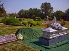 A Casket With Flowers Sits Beside A Gravesite Ready For Burial.