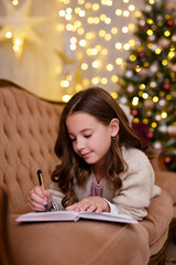 Wall Mural - cute little girl lying on sofa and writing letter to Santa Claus  in decorated living room with Christmas tree and lights