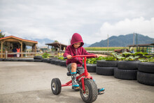Young Boy Wearing Hoody Pedals Oversized Tricycle On Racetrack.