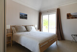Fototapeta  - Modern, clean double bedroom with glass sliding doors and white bedding and wooden bed frame