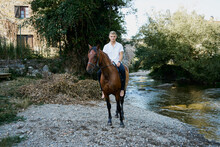 Portrait Of A Young Blond Man Riding A Horse Over A River