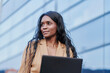 © Cavan Images - Portrait of black woman wearing a brown suit working on her laptop in the street