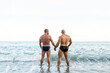 © Cavan Images - Lgbt pride concept. Muscled gay bear couple standing back on the shore of the beach. Holding hands and looking to the seascape.