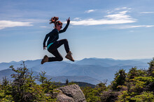 Young Athletic Woman Jumping Into Poses At Top Of Mountain.