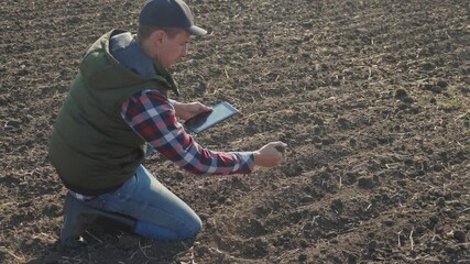 Wall Mural - man farmer red neck with a digital tablet walking on land for sewing on soil a black field lifestyle . eco agriculture farming concept. male worker studies winter dirt soil wheat crops works in field