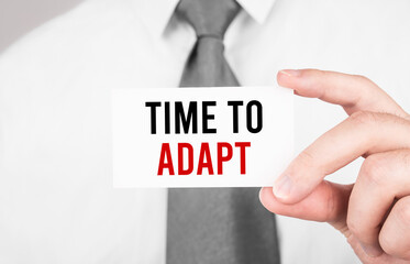 Businessman holding a card with text TIME TO ADAPT ,business concept