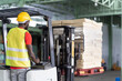 © amorn - African American male warehouse worker in safety vest and helmet driving and operating on forklift truck for transfer products or parcel goods in the industrial storage warehouse. multicultural worker