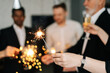 © dikushin - Close-up view of business team of multinational employees holding Bengal lights and smiling cheerfully at corporate New Year or Happy Christmas eve.