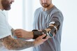 © Photographee.eu - Tattooed physiotherapist who puts an orthosis on the hand of a young patient after an accident