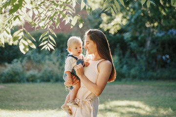 mothers day. young smiling caucasian mother and boy toddler son hugging in park. mom holding carryin