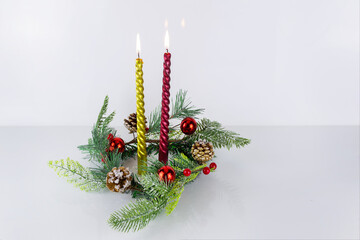 Two burning Christmas candles, gilded and red, in wreath of fir branches with cones.