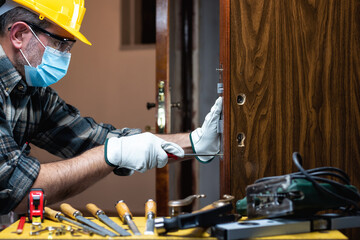 Wall Mural - Carpenter worker at work repair and install a room door lock, wear the surgical mask to prevent Coronavirus infection. Preventing Pandemic Covid-19 at the workplace. Carpentry.