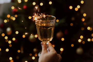 Wall Mural - Burning firework in champagne glass on background of christmas tree with lights