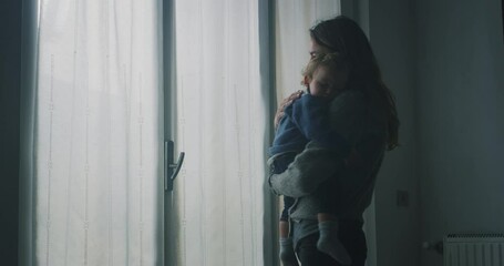 Wall Mural - Cinematic shot of an young peaceful mother is cuddling her toddler baby boy while sleeping on her arms at window with daylight. Concept of sweet dreams,childhood, life, motherhood.