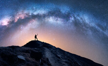 Arched Milky Way And Happy Man On The Mountain At Night. Silhouette Of Guy With Raised Up Arm On The Hill, Sky With Stars, Yellow Light In Nepal. Galaxy. Space Landscape With Milky Way Arch. Travel