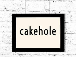 Black frame hanging on white brick wall with inscription cakehole