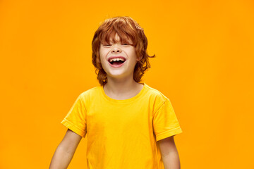 Wall Mural - Happy child laughs on a yellow background red hair T-shirt 