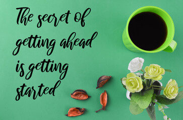 Top view of leaves, flowers and a cup of coffee over a green background written with text THE SECRET OF GETTING AHEAD IS GETTING STARTED. Motivational concept.
