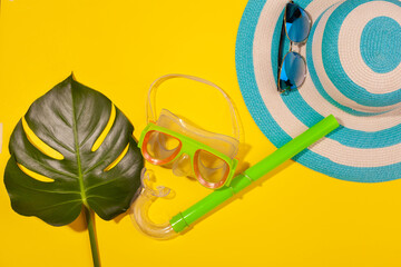 Wall Mural - Top view on beach accessories on yellow background - sunglasses, striped blue hat, diving mask and monstera leaf. Concept of the long-awaited vacation at sea and travel. Advertising space