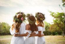 Young Women Wearing Wreaths Made Of Beautiful Flowers Outdoors On Sunny Day, Back View