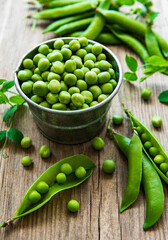 Fresh green peas in a small metal bucket on old wooden background.