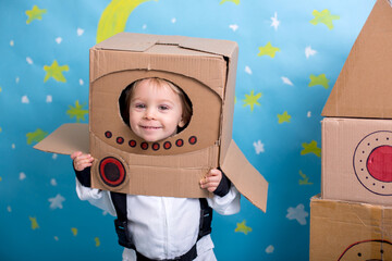 Sweet toddler boy, dressed as an astronaut, playing at home with cardboard rocket and handmade helmet