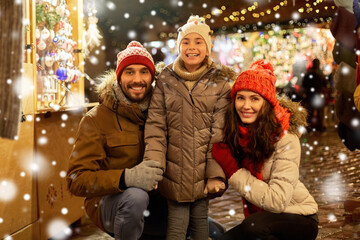 family, winter holidays and celebration concept - happy mother, father and little daughter at christmas market on town hall square in tallinn, estonia over snow