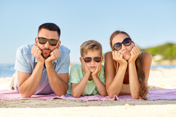 family, leisure and people concept - unhappy mother, father and little son in sunglasses lying on summer beach