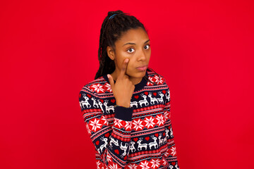 Wall Mural - Young beautiful African American woman standing against red background Pointing to the eye watching you gesture, suspicious expression.