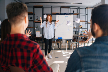 Wall Mural - Dissatisfied colleagues throw crumpled paper balls at frightened woman coworker. Cheerful young business lady finishing report on white board. Confused female runs away and hides behind blackboard.