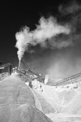 Wall Mural - High column of white dust on the background of black sky over rock stone crushing equipment at the limestone quarry, black and white image.