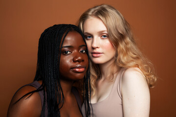 two pretty girls african and caucasian blond posing cheerful together on brown background, ethnicity diverse lifestyle people concept