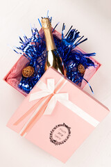 Wall Mural - a gold bottle of champagne lies in a pink gift box with a bow and blue Christmas tinsel on a white table background