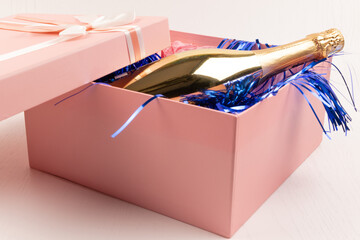 Wall Mural - a gold bottle of champagne lies in a pink gift box with a bow and blue Christmas tinsel on a white table background