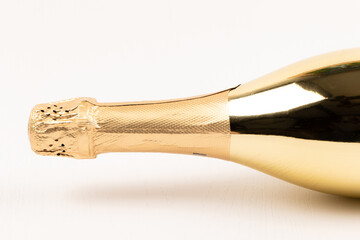 the neck of a festive champagne bottle sealed with gold foil on a white wooden table background