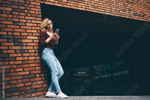 Fotografía Pretty blonde woman in stylish casual clothes surfs internet with modern smartphone in city street on sunny summer day
