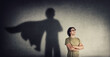 © 1STunningART - Confident young man keeps arms crossed smiling optimistic as casting a superhero with cape shadow on the wall. Motivated and ambitious guy tends to achieve success. Hero leadership and power concept