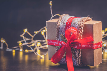 Brown present box or gift box package in craft paper and Christmas decorations over dark background, side view. Christmas and New Year holidays background with copy space. Christmas shopping concept.