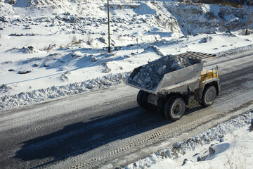 Wall Mural - Heavy mining truck transports stone ore against the background of a snow-covered quarry in sunny weather, close-up.