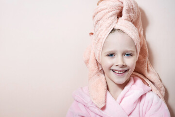 Wall Mural - a little girl with blue eyes in a pink robe and a pink towel on her head after a bath smiles and loo