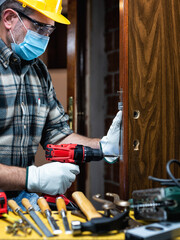 Wall Mural - Carpenter worker at work repair and install a room door lock, wear the surgical mask to prevent Coronavirus infection. Preventing Pandemic Covid-19 at the workplace. Carpentry.