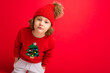 © Ivan Traimak - cute blond boy in warm hat and christmas sweater on red background with smile on his face