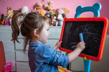 Three-Year-Old Girl Drawing With Chalk On The Blackboard