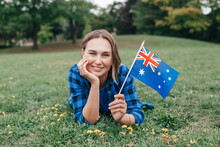 Happy Caucasian Middle Age Woman Waving Australian Flag. Smiling Proud Citizen Lying On Green On Grass Ground In Park Celebrating Australia Day Holiday In January Outdoors.