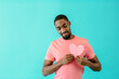 © Carlos David - Portrait of a serious  young man in love, holding pink heart with eyes closed, isolated on blue copy space