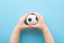 Baby Boy Hands Holding And Playing With White Black Football Ball On Light Blue Floor Background. Pastel Color. Closeup. Toys Of Development For Infant. Point Of View Shot. Top Down View.