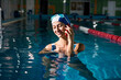 © DmitryStock - Woman swimmer in a swimming cap holds a phone in her hands, stands in a sports pool