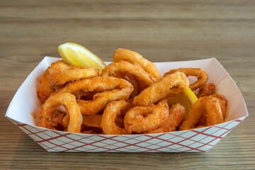 deep fried calamari (squid) rings in a take out tray with pieces of lemon