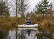 © ANDA - gray and cloudy day, fisherman in a white boat, river bank with bare trees and bushes, shore reflection in river water