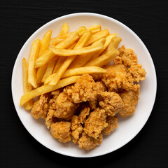 Homemade Fried Chicken Bites and French Fries on a plate on a black surface, top view. Flat lay, overhead, from above. Close-up.